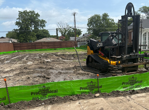 Skid steer parked next to a freshly installed silt fence on a grassy job site in Texas.