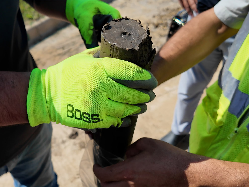 Construction crew carefully hands a cylindrical soil core sample to the geotechnical engineer, maintaining chain of custody