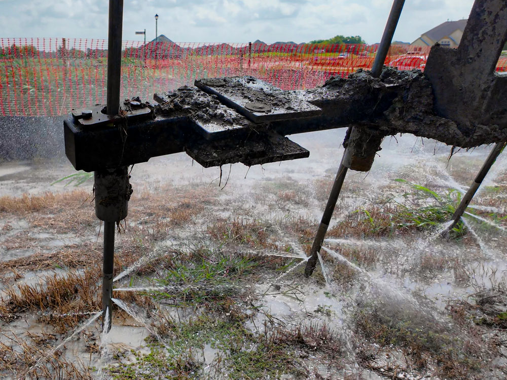 Close-up of soil injection rods spraying high-pressure water horizontally into the subgrade during ProChemical’s treatment process.