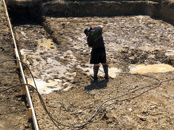 Technician performing hand injection soil stabilization inside a pool excavation site, using pressurized solution to treat expansive clay soil before concrete pour.